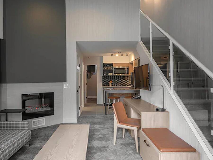 Ein modernes Wohnzimmer mit Sofa, Couchtisch und Kamin. Eine Treppe führt zu einer Küchenzeile mit Esstisch und Stühlen.