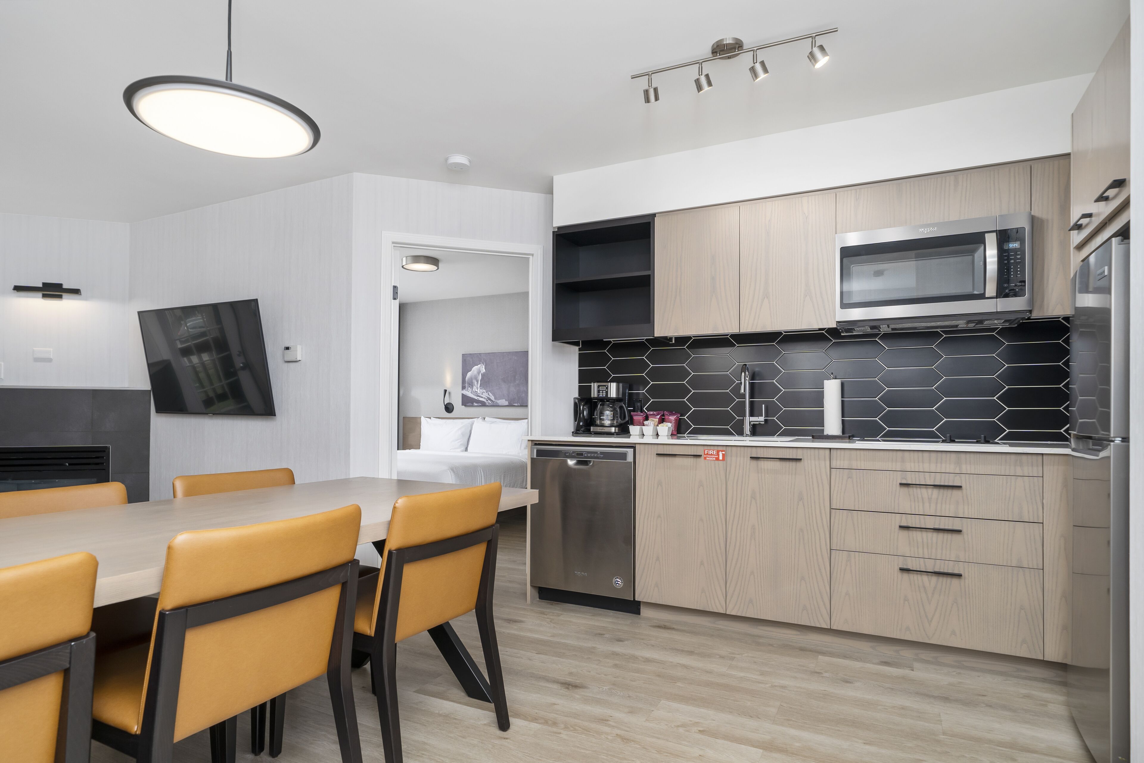 A modern kitchen with a dining area, featuring a flat-screen TV, a built-in microwave, and a coffee machine.