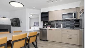 A modern kitchen with a dining area, featuring a flat-screen TV, a built-in microwave, and a coffee machine.