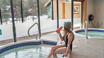 A person sitting in a hot tub with a view of the outdoors through large windows.