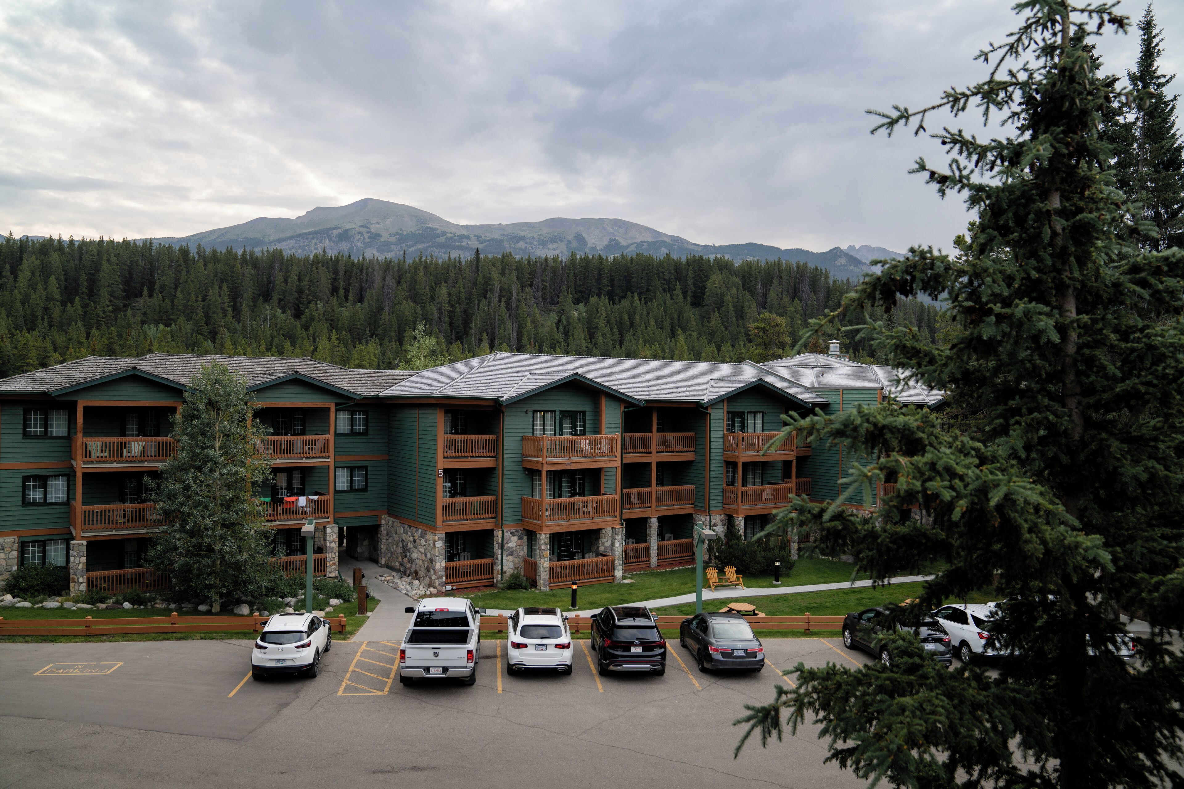 A multi-story hotel with balconies, a parking lot, and a mountainous backdrop.