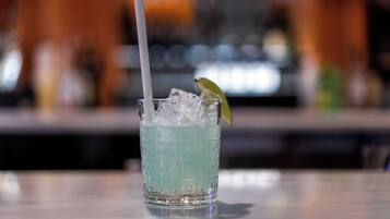 A glass of blue beverage with ice cubes and a lime wedge, placed on a bar counter.