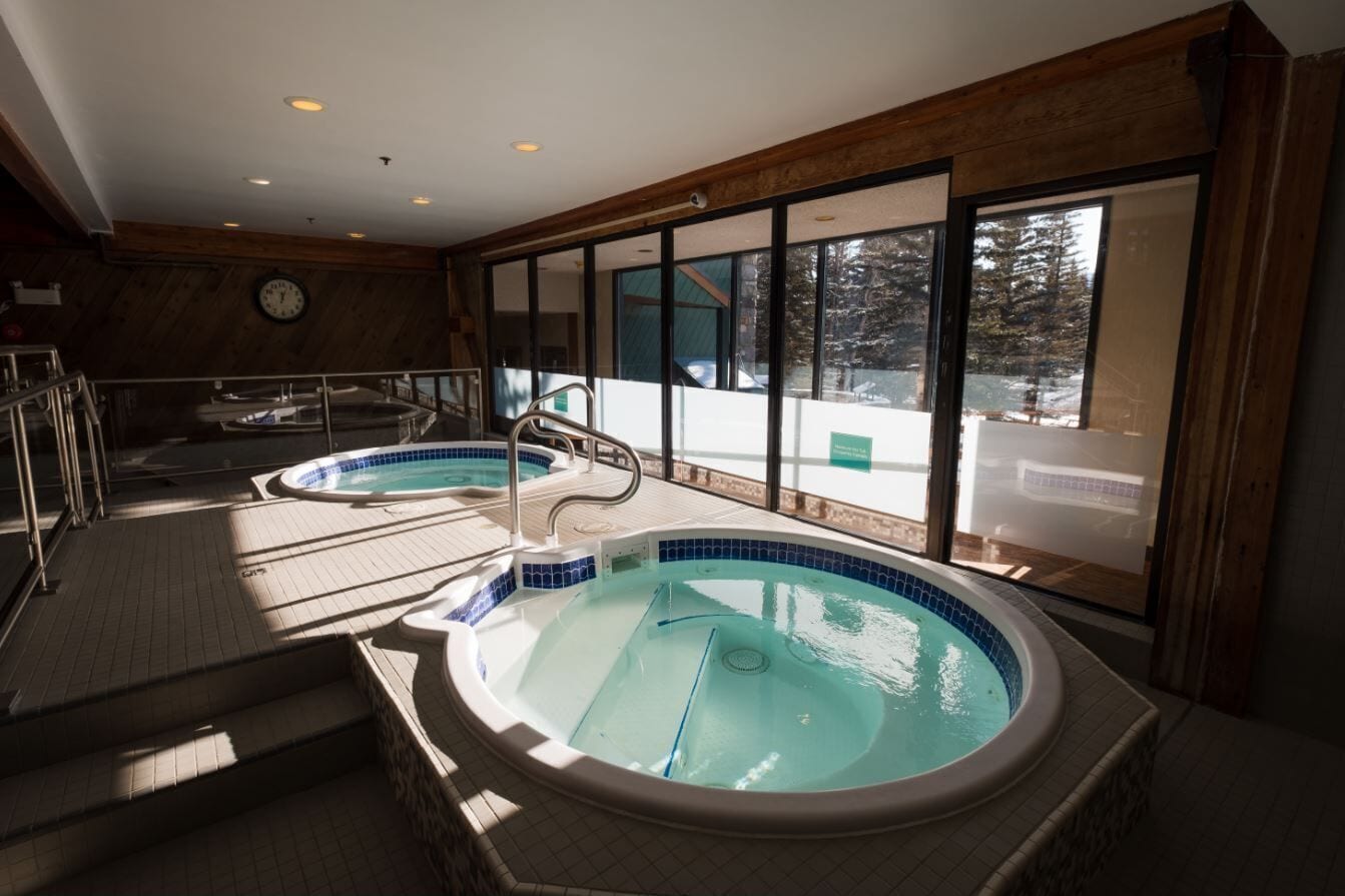 Ein Wellnessbereich mit zwei Whirlpools, Holzverkleidung und großen Fenstern.
