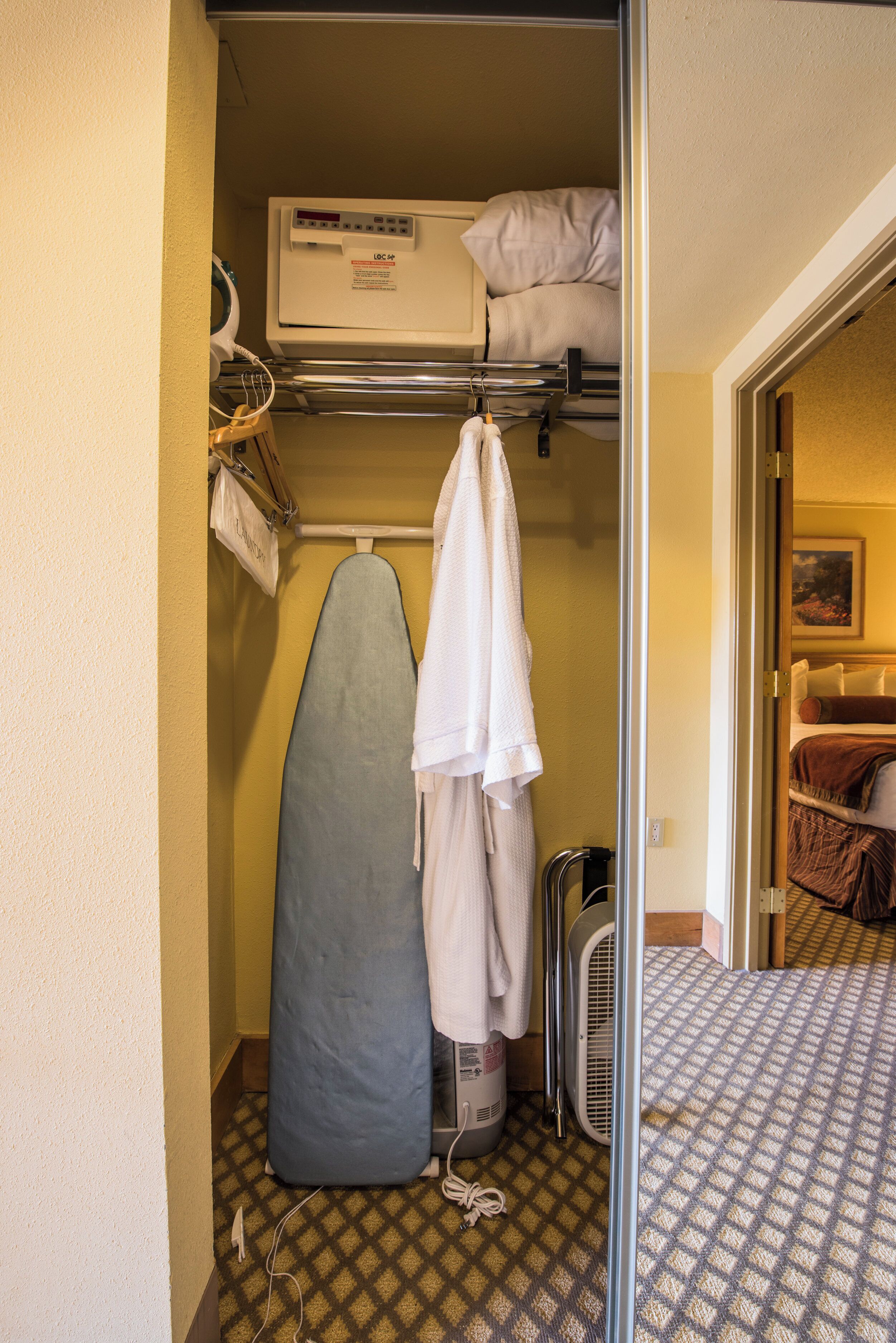 Habitación de hotel pequeña con una litera, una tabla de planchar, un ventilador y una alfombra estampada.