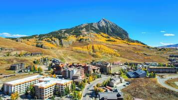 A town with a prominent mountain in the background, featuring a mix of modern and traditional buildings, a central road, and a parking area.