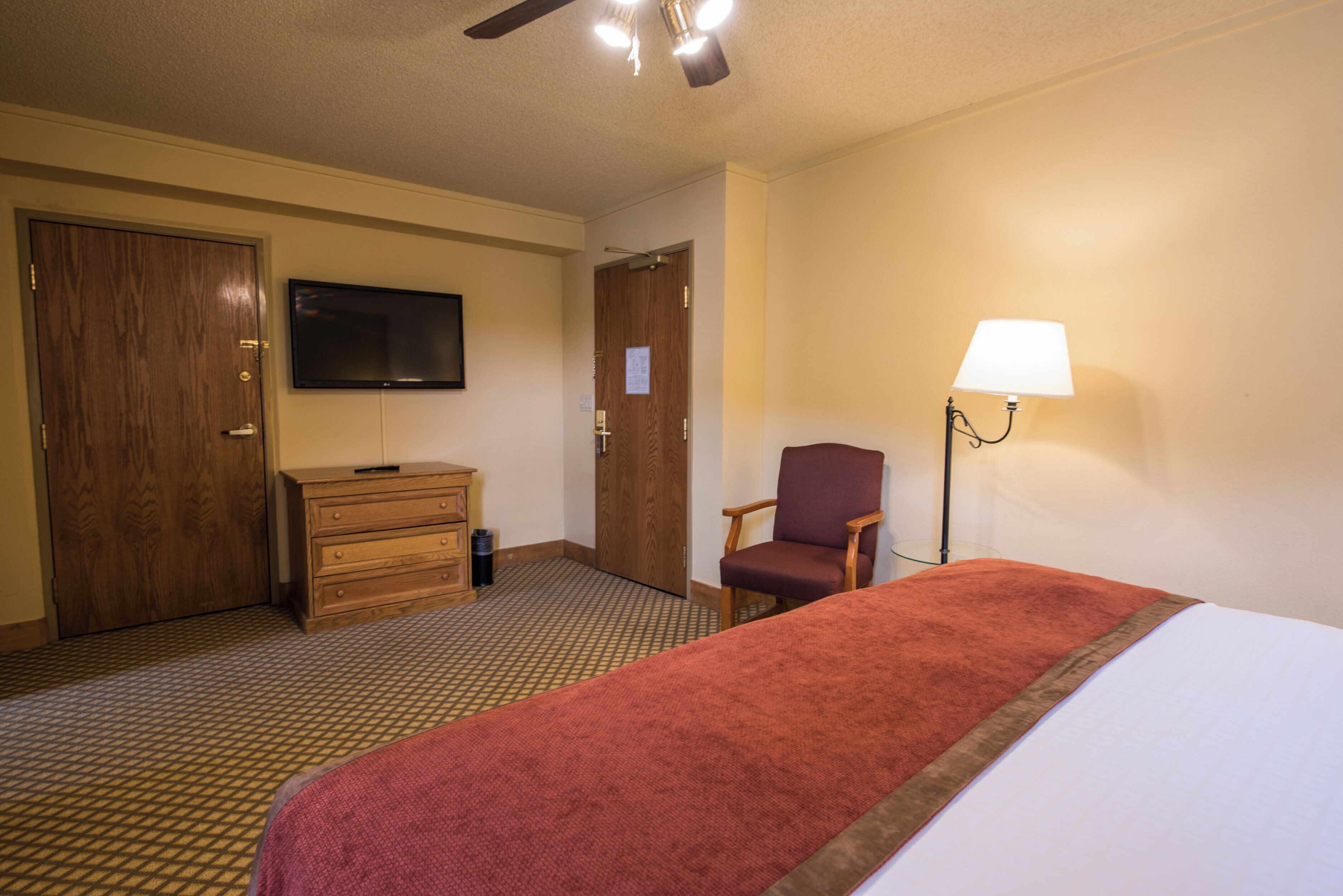 Ein Hotelzimmer mit einem Bett, einem Fernseher, einem Schreibtisch, einem Sessel und einer Lampe.