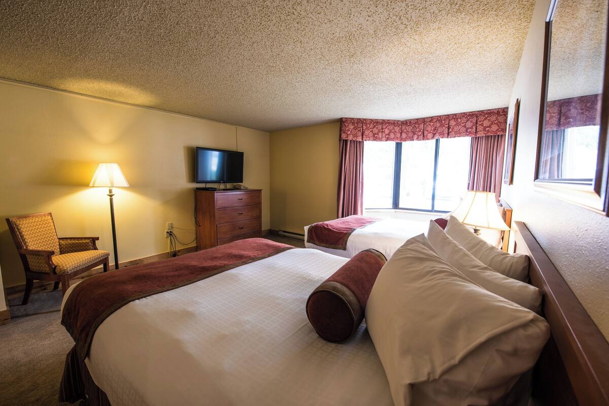 A hotel room with two beds, a television, a lamp, and a chair.