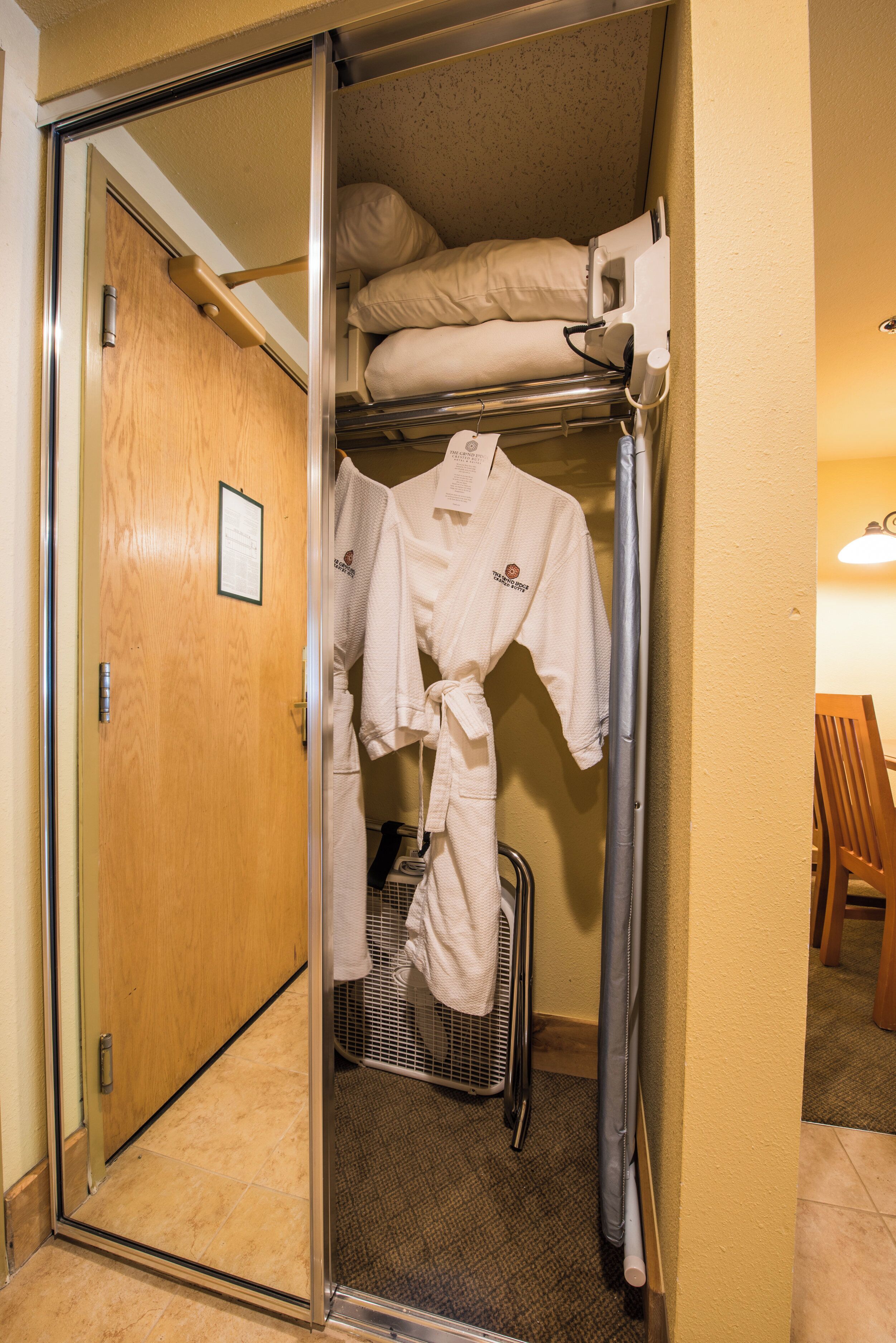 A hotel room with a wooden door, a metal rack with robes, and a small heater on the floor.
