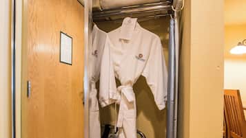 A hotel room with a wooden door, a metal rack with robes, and a small heater on the floor.
