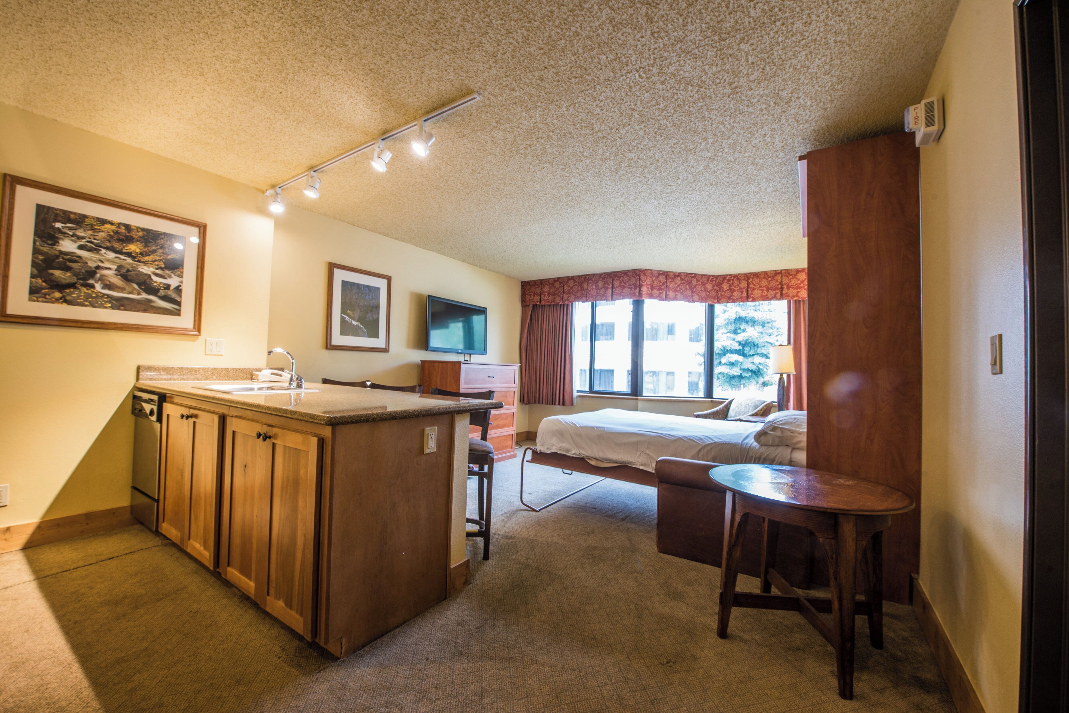 Une chambre d’hôtel équipée d’une kitchenette, d’un lit, d’un bureau et d’une fenêtre avec des rideaux.