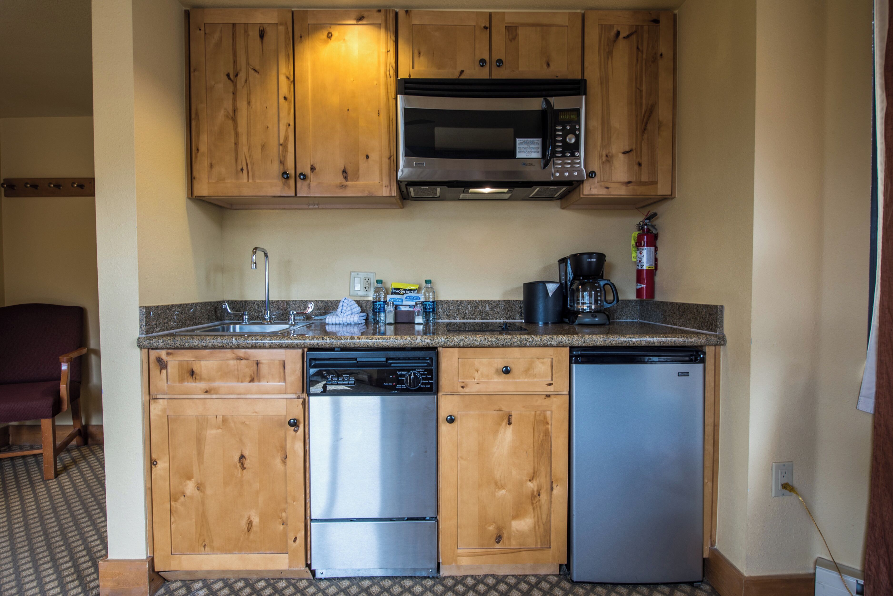 Cocina compacta con armarios de madera, lavavajillas de acero inoxidable, microondas y cafetera.
