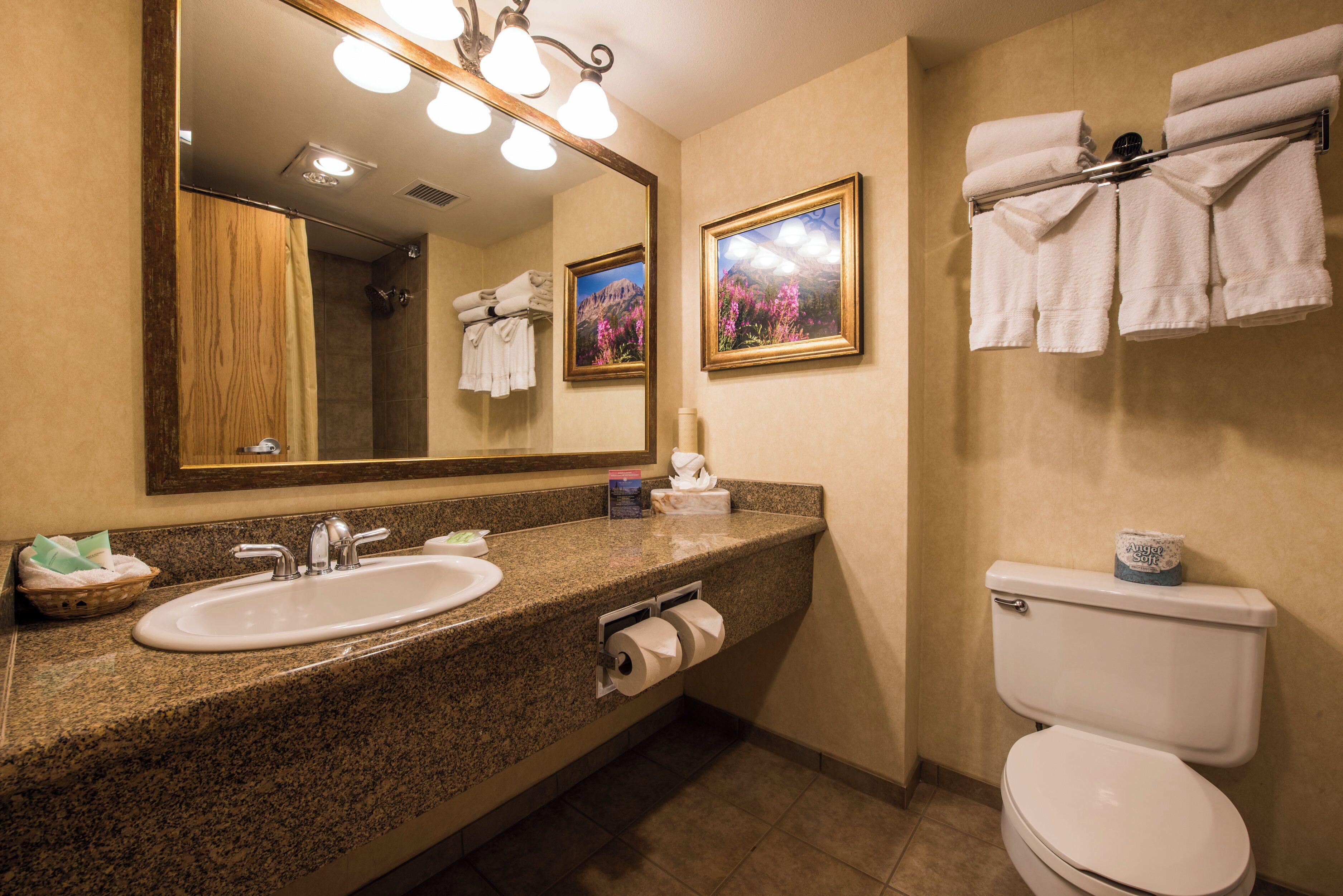 A bathroom with a granite countertop sink, a mirror, a toilet, and a towel rack with folded towels.
