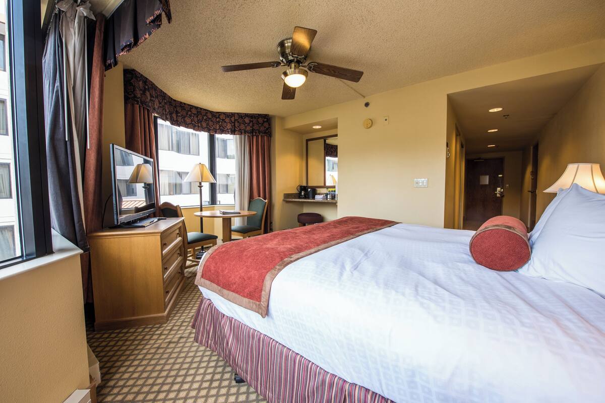 A hotel room with a bed, a desk, a chair, a television, and a ceiling fan.
