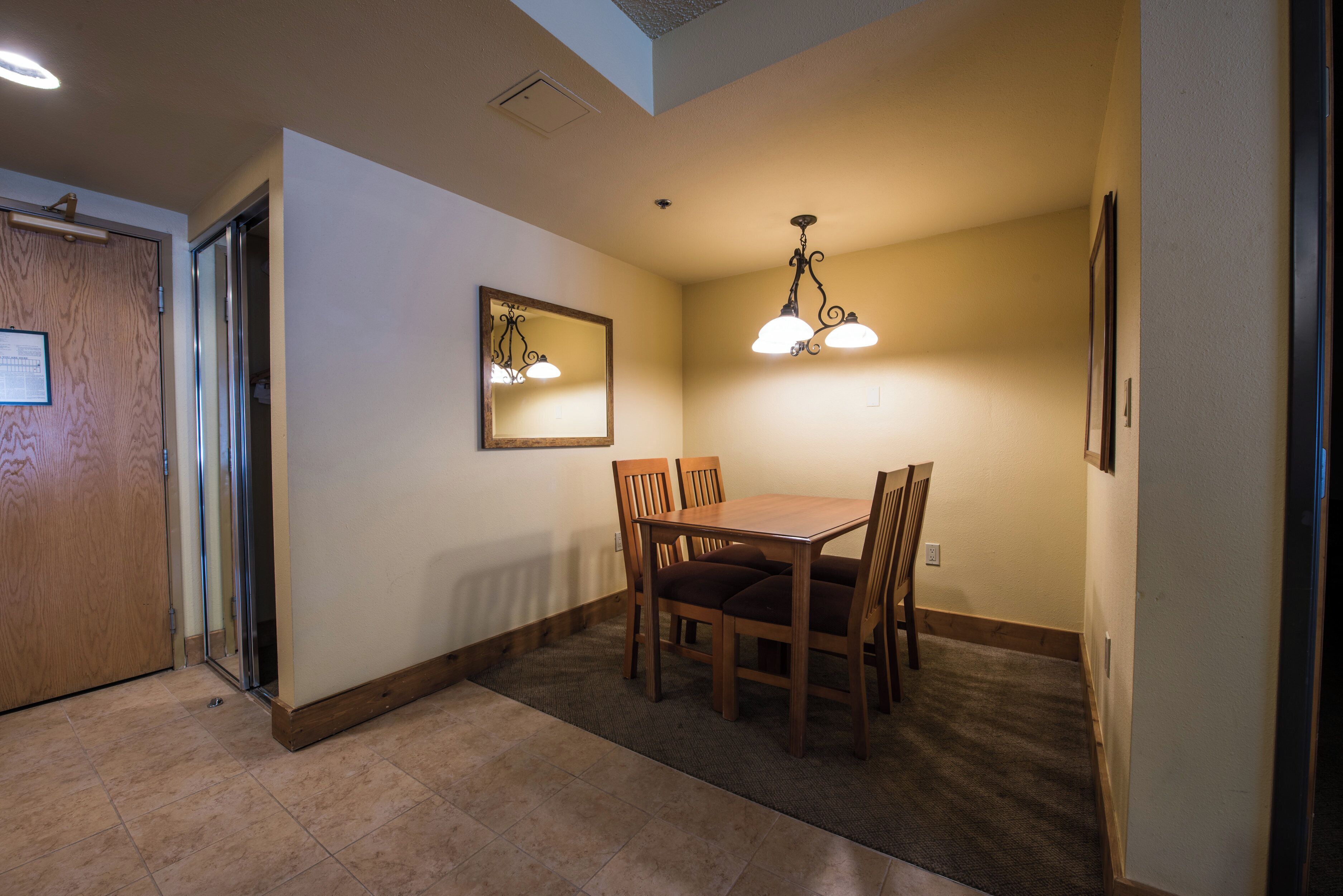 A dining area with a wooden table and chairs, a mirror on the wall, and a ceiling light fixture.