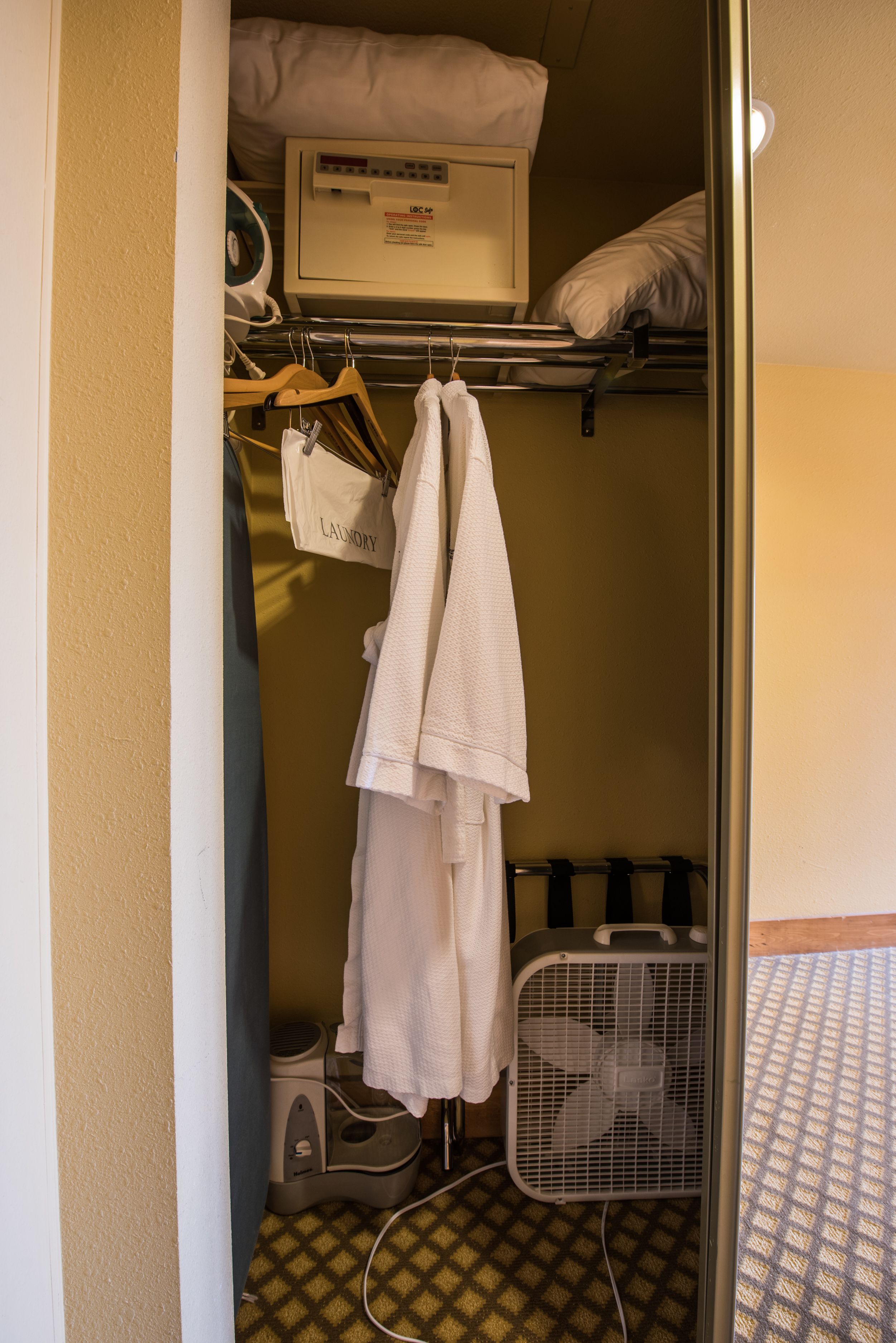 A compact bathroom with a shower stall, a towel rack with hanging towels, a portable heater, and a small laundry bag labeled "LAUNDRY".