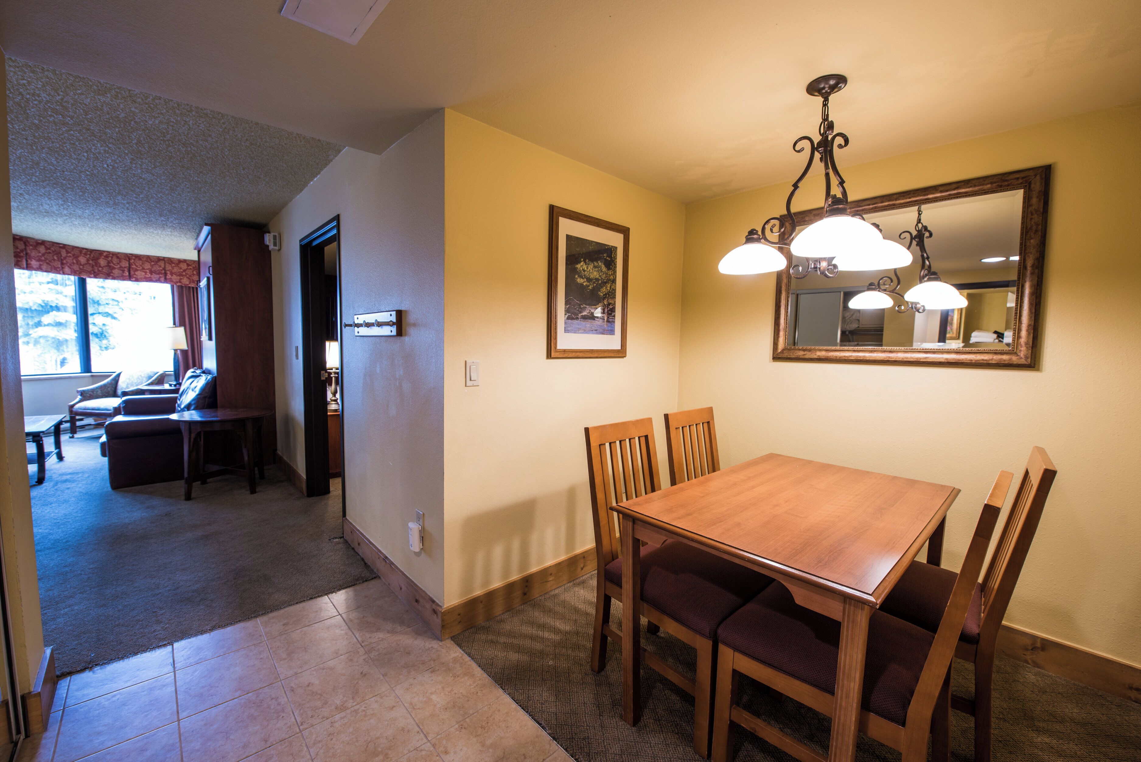 A dining area with a wooden table and chairs, a chandelier, and a mirror on the wall.