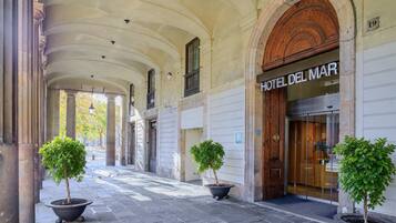 A hotel entrance with a classic arched doorway, a sign reading 'HOTEL DEL MAR', and potted plants along the walkway.