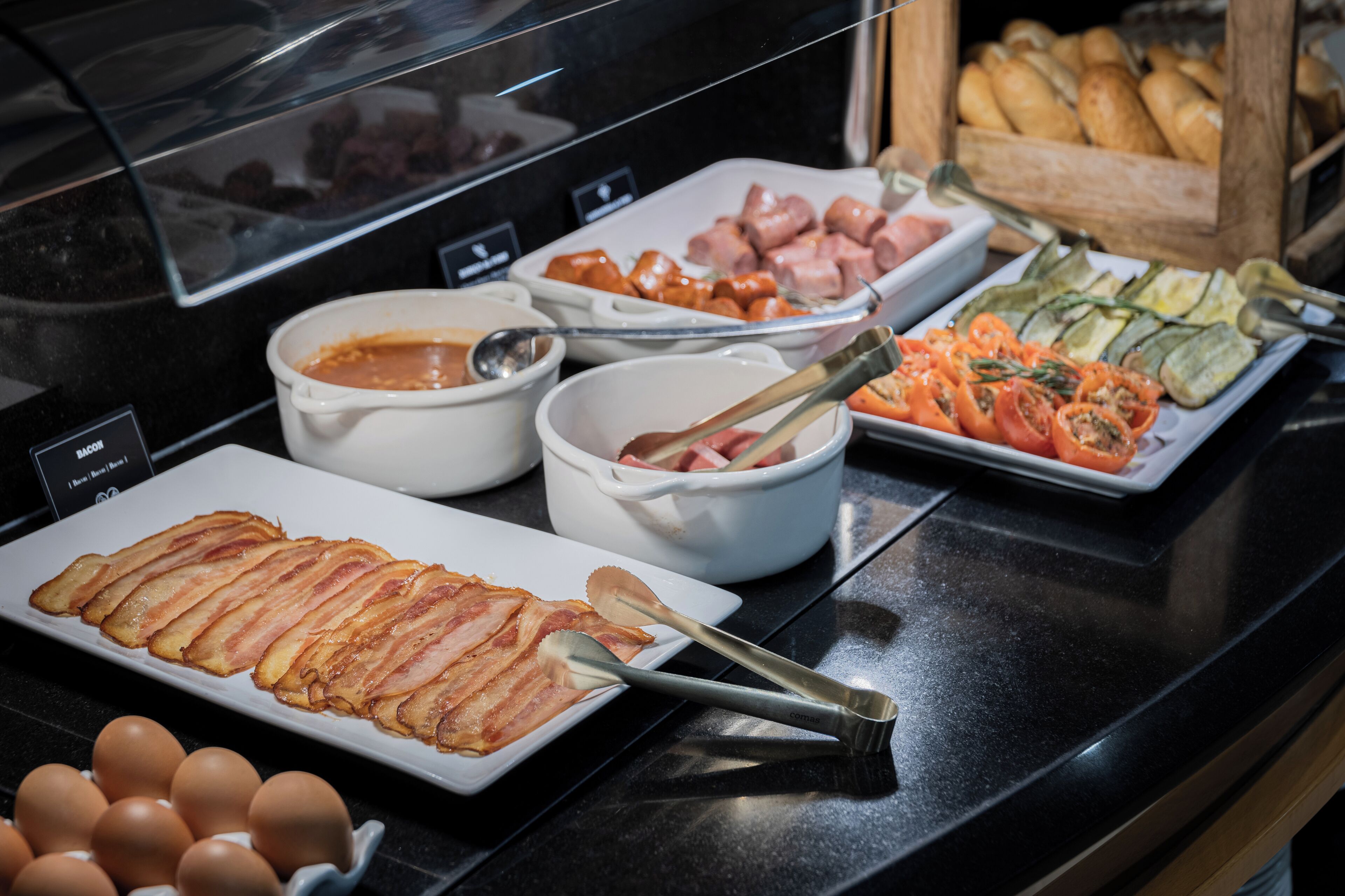 Un buffet proposant une variété de plats, notamment du bacon, des œufs et des légumes.