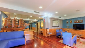 A modern hotel lobby with a wooden ship model, blue sofas, a TV, and a reception desk. - Hotel Del Mar (Barcelona)
