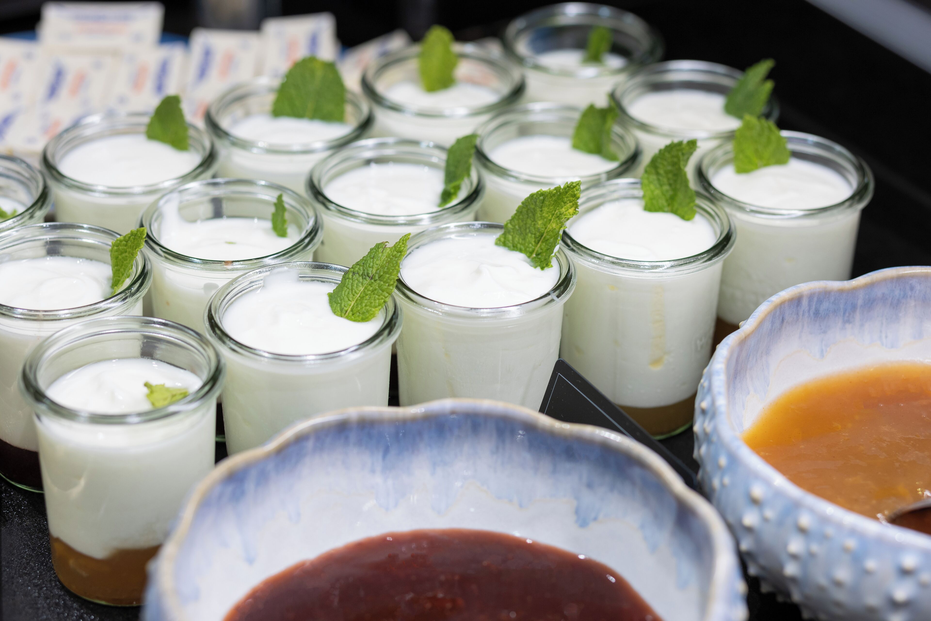 Une présentation de petits pots en verre remplis d’une substance crémeuse blanche, décorés de feuilles de menthe, et accompagnés d’un bol de sauce brune.