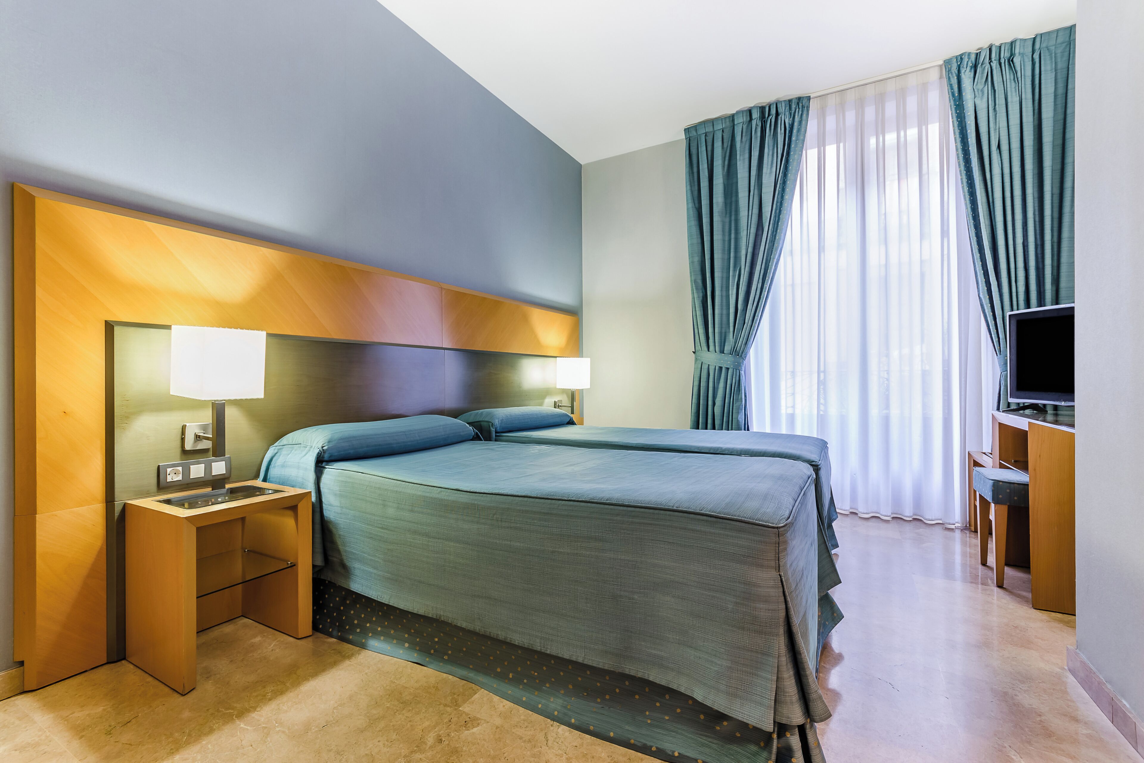 Une chambre d’hôtel comprenant un lit, des tables de chevet, un bureau avec une chaise et un téléviseur.