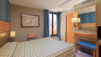 Habitación de hotel con cama, escritorio, silla, televisor y un amplio ventanal con cortinas.