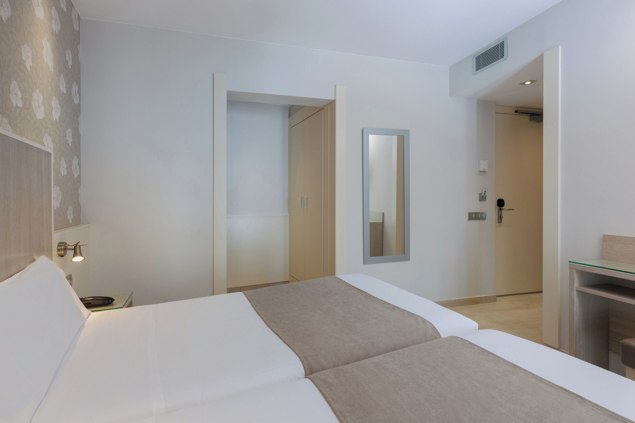 Une chambre d’hôtel moderne avec un grand lit, une table de chevet, un miroir et une vitrine.