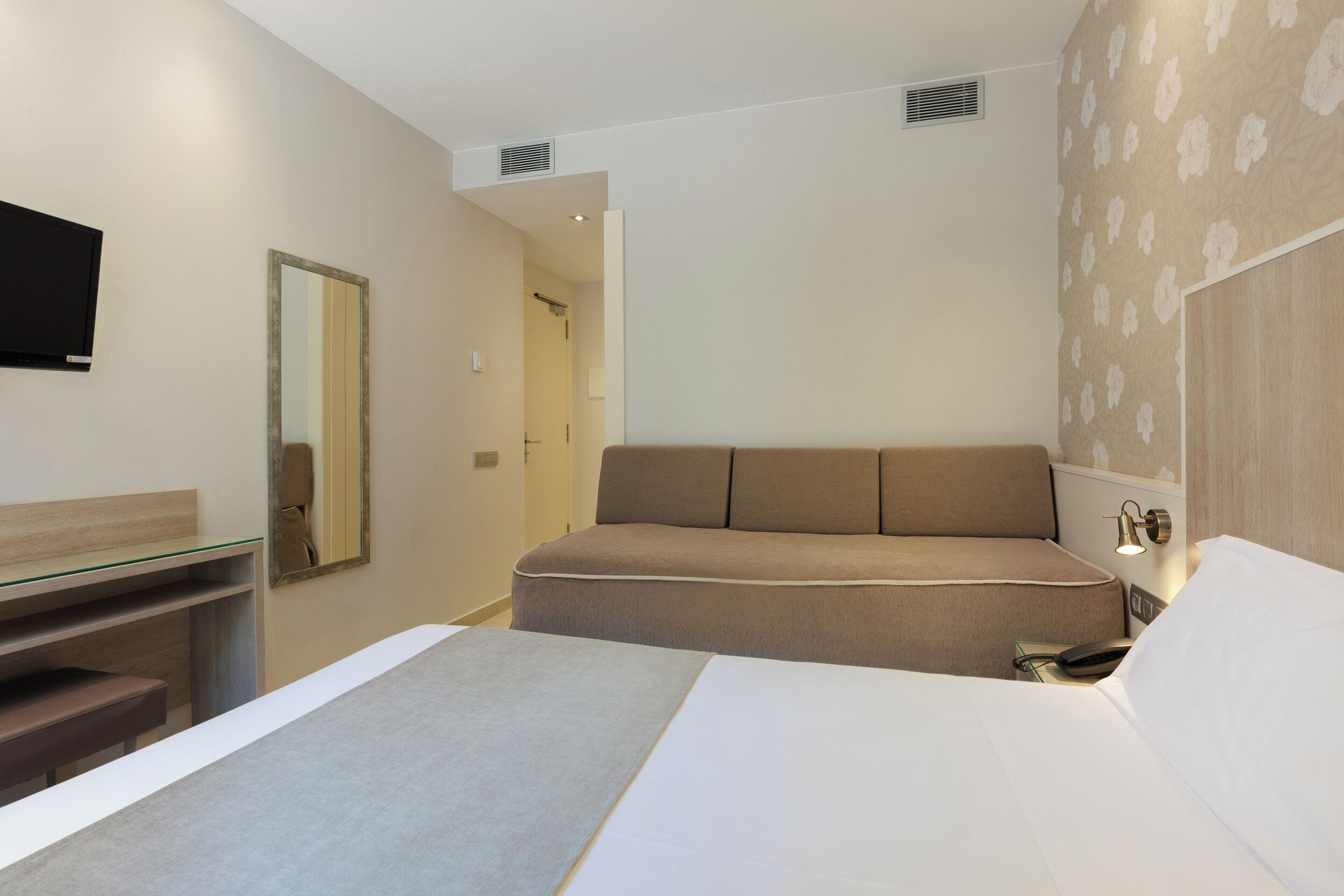 Une chambre à coucher moderne avec un lit, un canapé, une table de chevet, un miroir et un téléviseur.