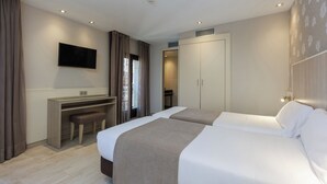 Habitación de hotel con dos camas, un escritorio, un televisor y un armario.