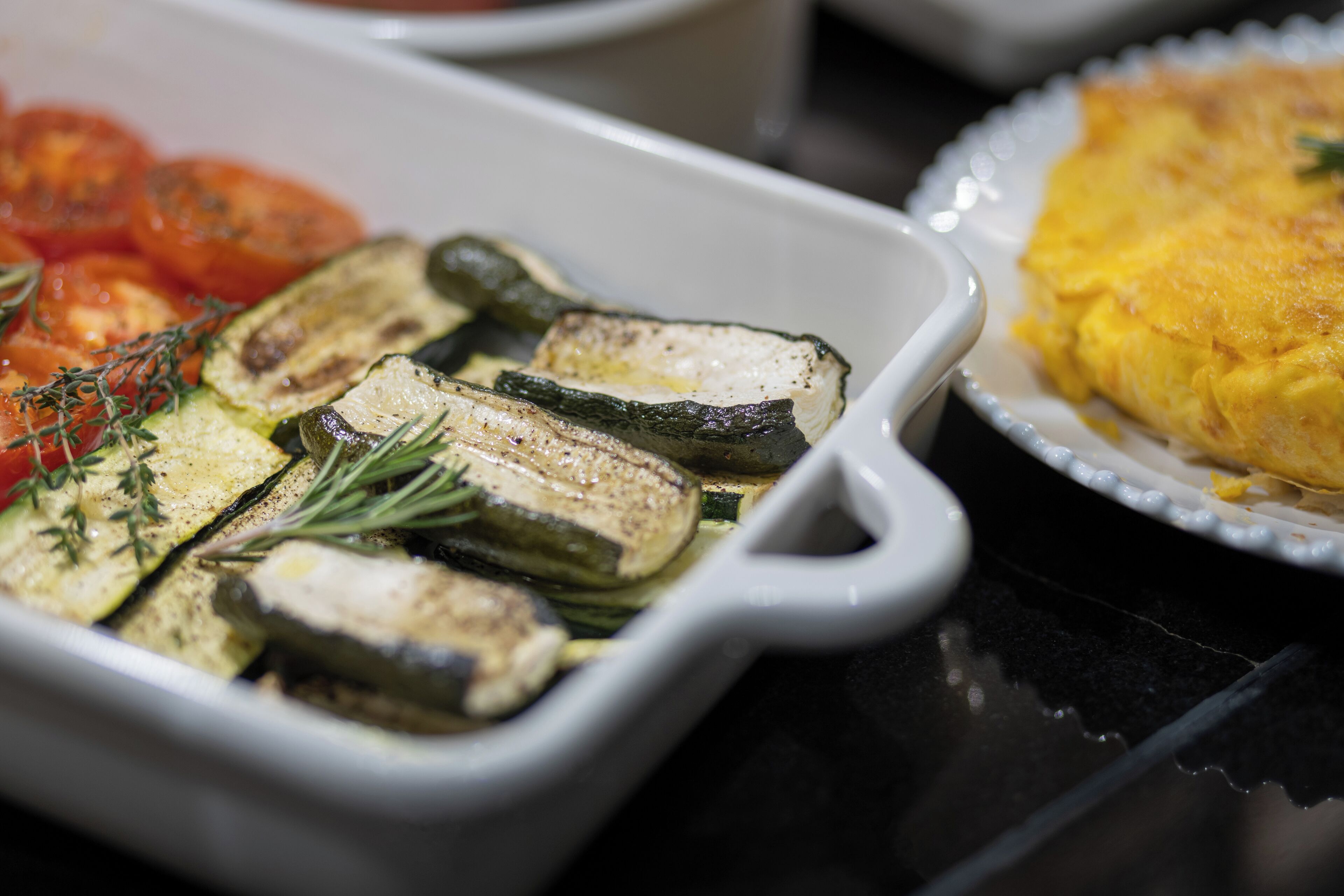 Un plato de cerámica blanca con verduras asadas y una guarnición de huevos revueltos.