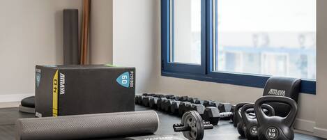 Un gimnasio con equipo de levantamiento de pesas, incluyendo mancuernas y kettlebells, y una colchoneta de yoga.