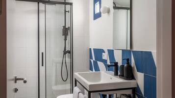 Une salle de bain moderne avec une douche à parois de verre, des carreaux blancs, un lavabo blanc et des carreaux bleus à motifs géométriques sur le mur.