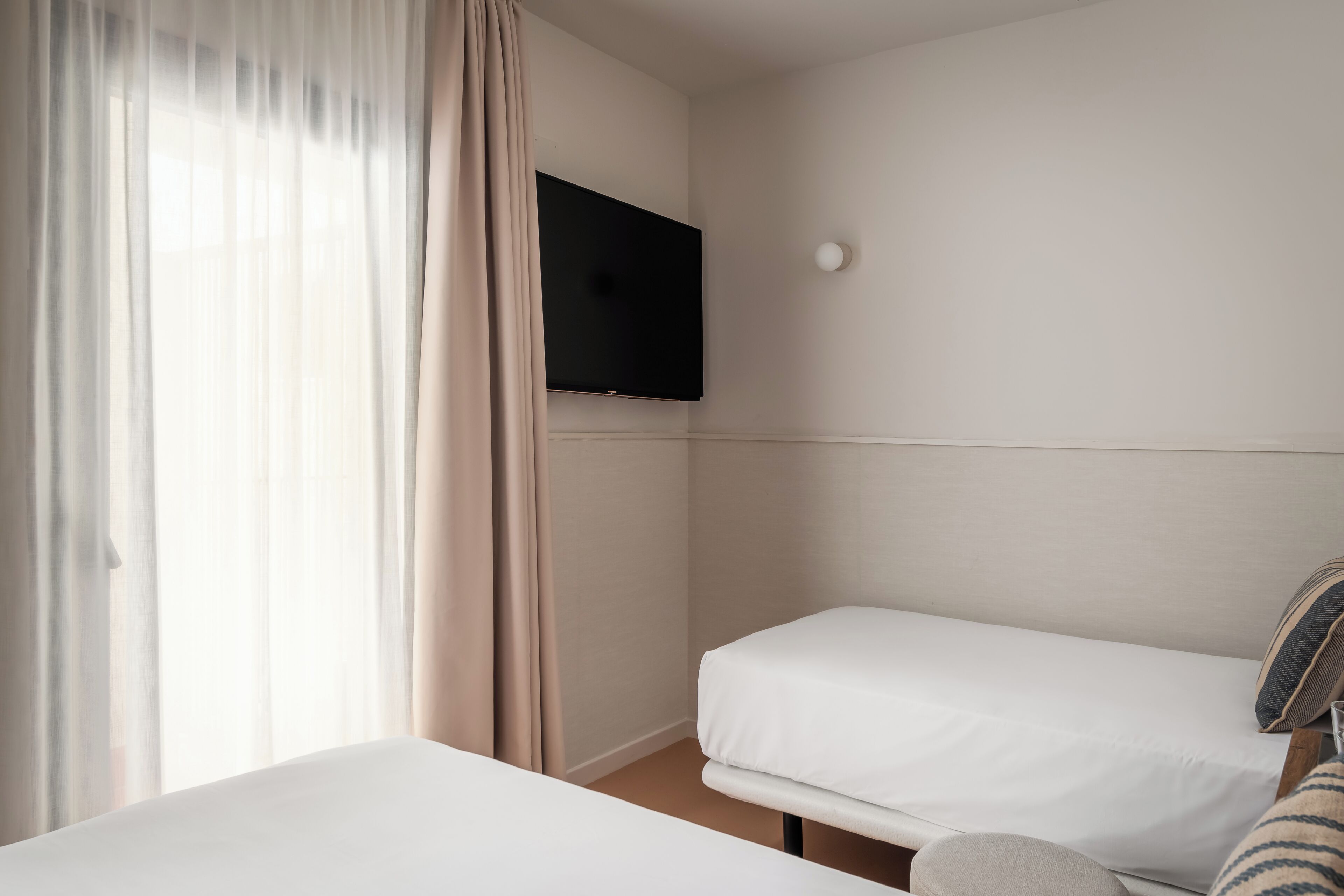 Habitación de hotel con cama, televisor montado en la pared y ventana con cortinas.