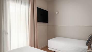 A hotel room with a bed, a TV mounted on the wall, and a window with curtains.