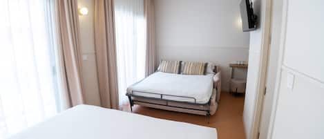 Un dormitorio con cama, cortinas, un televisor instalado en la pared y una mesita con vasos.