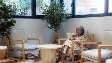 Ein Zimmer mit großem Fenster, einem Blumentopf und einer Person, die ein Buch liest.
