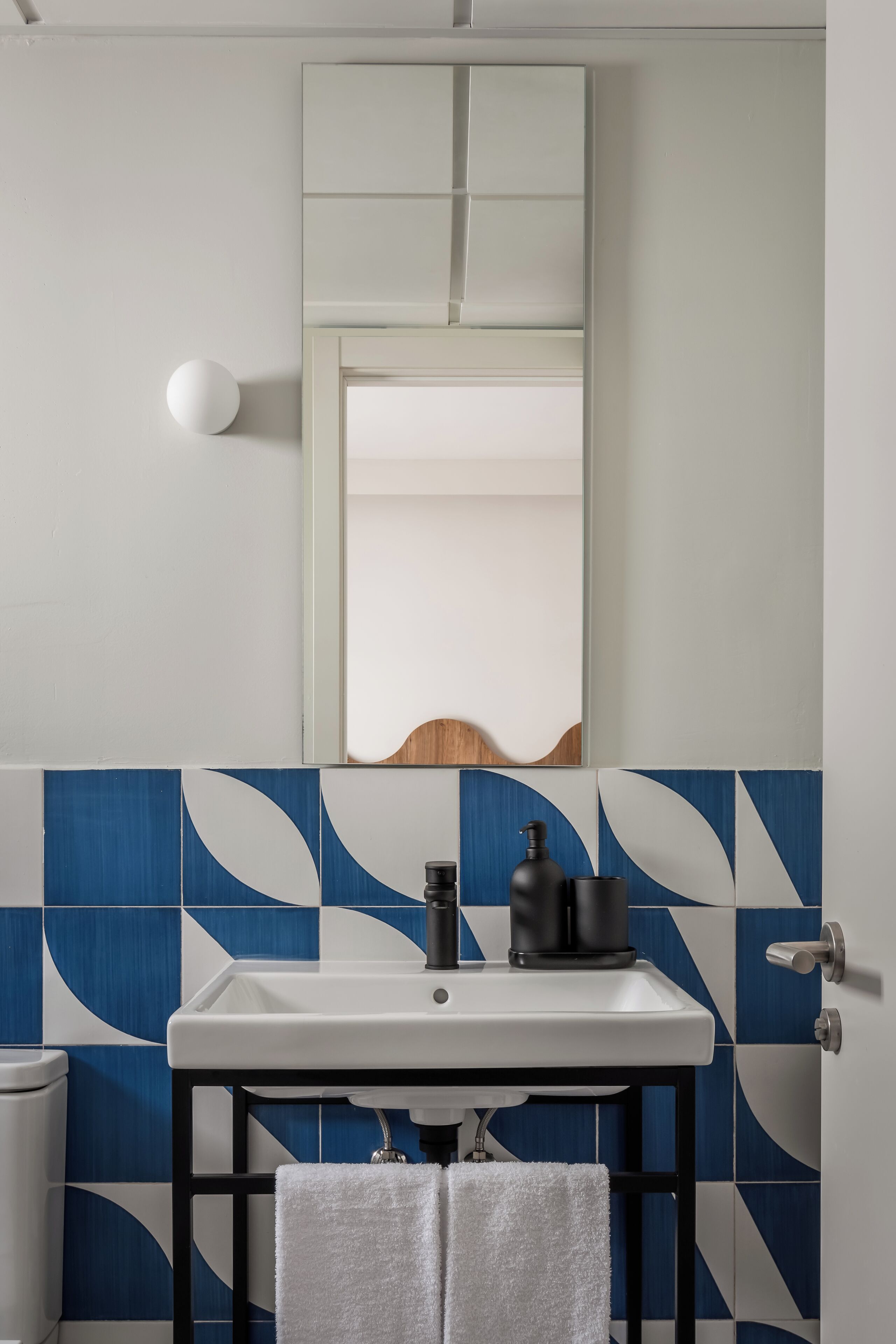 A bathroom with a white sink, black faucet, and a mirror above it. The wall has blue and white tiles.