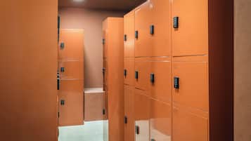 Una hilera de taquillas naranjas con puertas numeradas, un suelo de tonos claros y una lámpara empotrada en el techo.