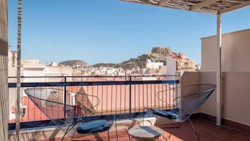 Un balcón con dos sillas de estructura metálica y una pequeña mesa redonda, con vista a un paisaje urbano que incluye una colina destacada al fondo.