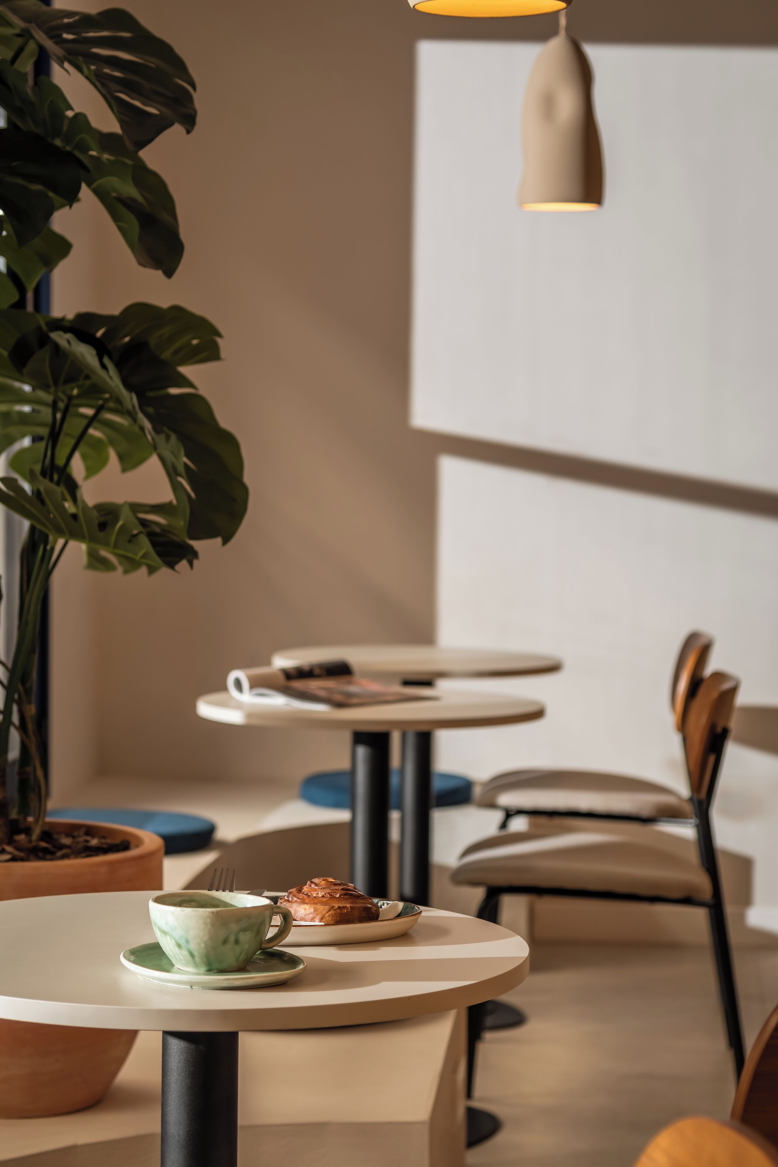 Un café avec des tables rondes, des chaises, une plante en pot et un luminaire suspendu.