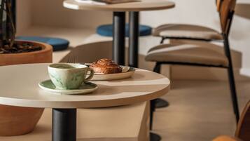 Un café avec des tables rondes, des chaises, une plante en pot et un luminaire suspendu.