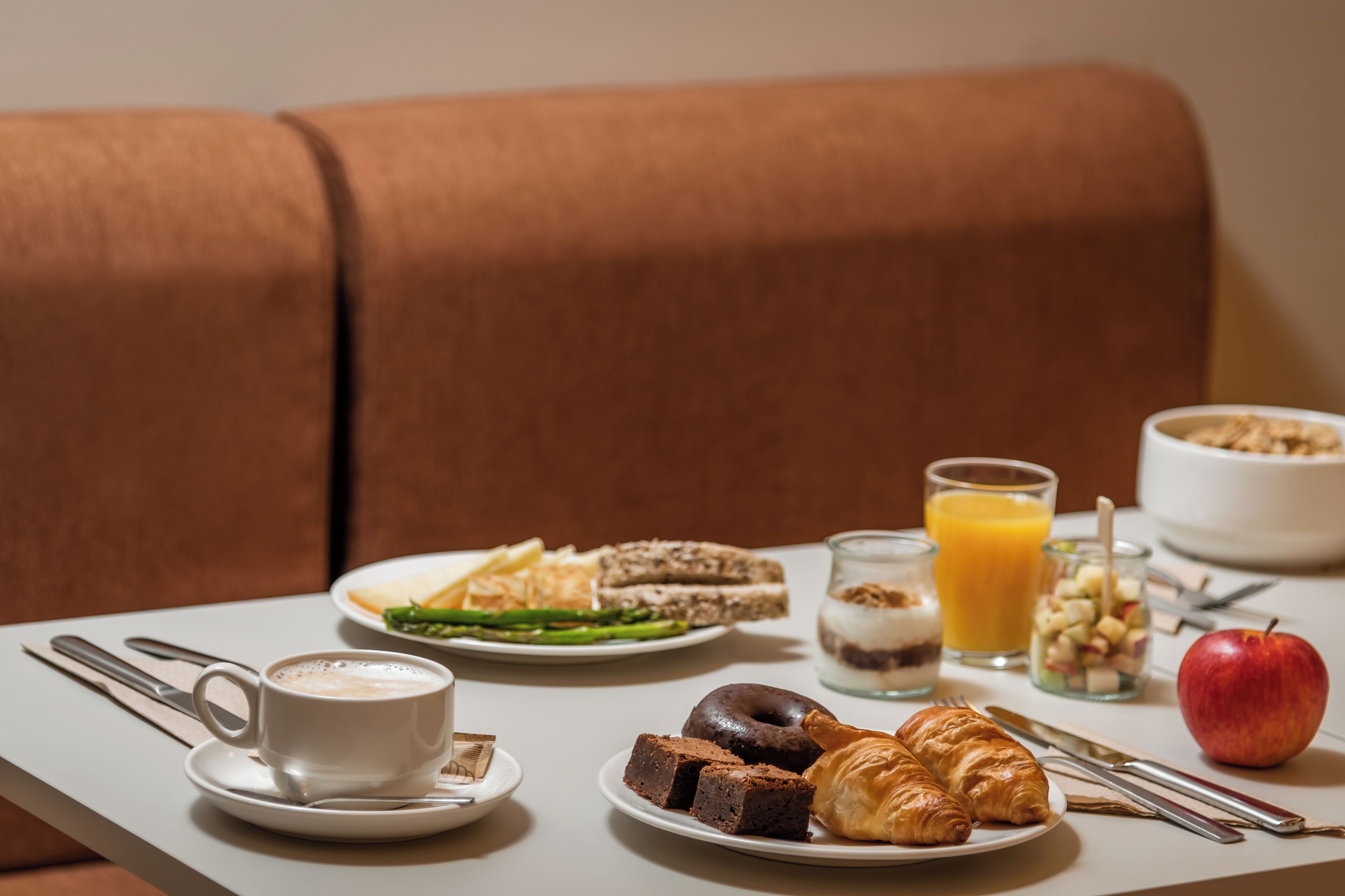 Een ontbijttafel met croissants, een croissantbroodje, een appel, een glas sinaasappelsap en een kom ontbijtgranen.