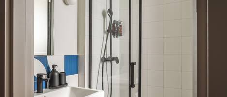 A modern bathroom with a glass-enclosed shower, a white sink with a soap dispenser, and a mirror above the sink.