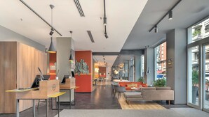 A modern hotel lobby with a reception desk, seating area, and large windows offering views of the city. - B&B Hotel Milano Central Station (Milan)