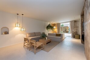 Relax in this stylish living room with a sofa set, coffee table, and wooden chair, surrounded by a neutral color palette and natural light.
