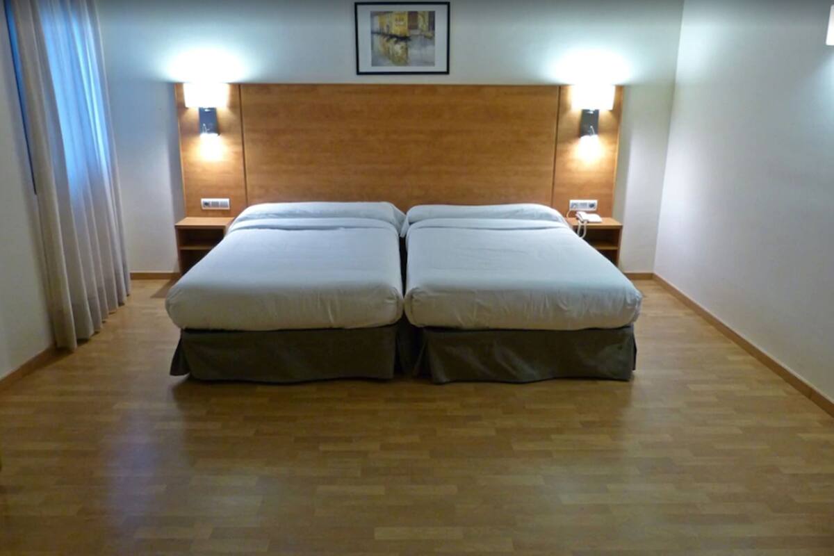 Habitación doble con dos camas, cabecero de madera, lámparas de noche y un cuadro enmarcado en la pared.