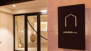 Entrada de un hotel con puerta de vidrio, un letrero con el icono de una casa y el nombre 'civenida HOTEL'.