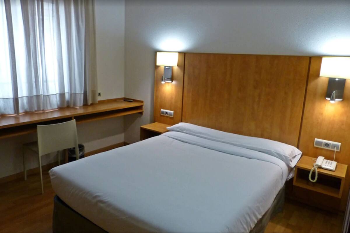 Una habitación de hotel con cama, escritorio, silla y lámparas de noche.