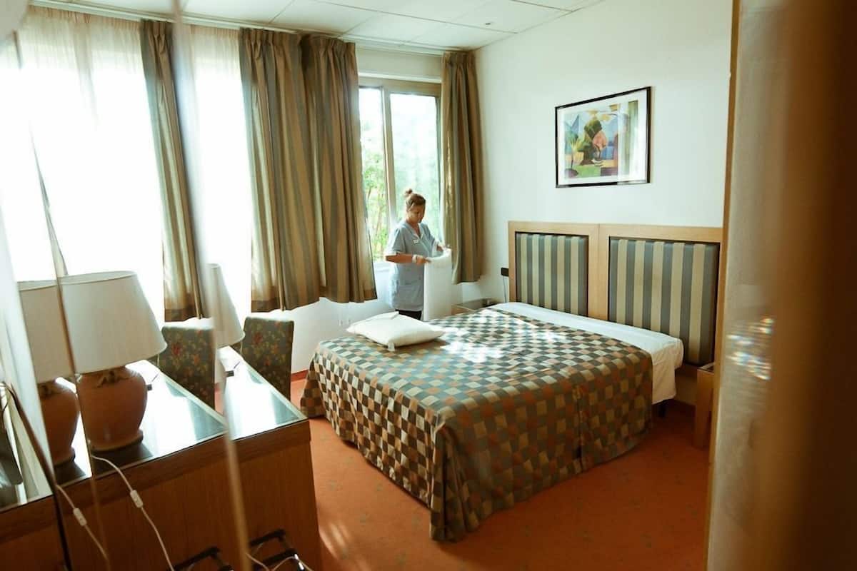 A hotel room with a bed, a desk, a chair, and a window with curtains.