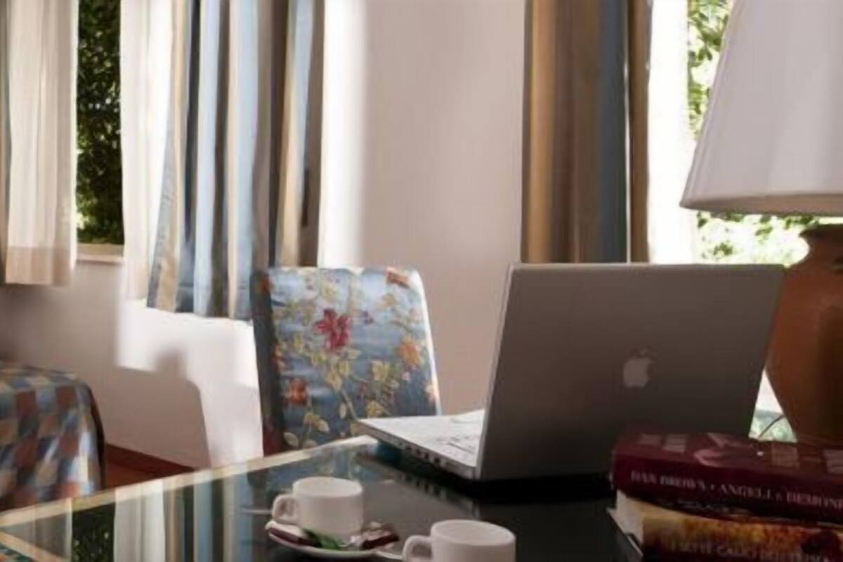 A hotel room with a checkered bedspread, a laptop on a table, and a window with curtains.